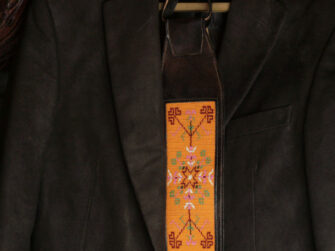 Leather tie is hanged onto the hanger with the gentleman's jacket. The beadwork on the centre of the tie is mostly yellow and features Estonian folk pattern.
