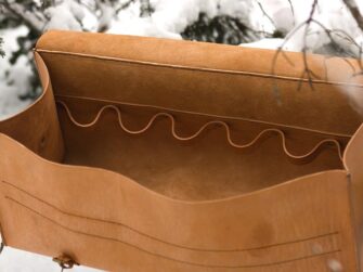 Very large leather bag is photographed in the snowy forest. Bag is set onto the fallen tree branch. This photo shows the inside of the bag.