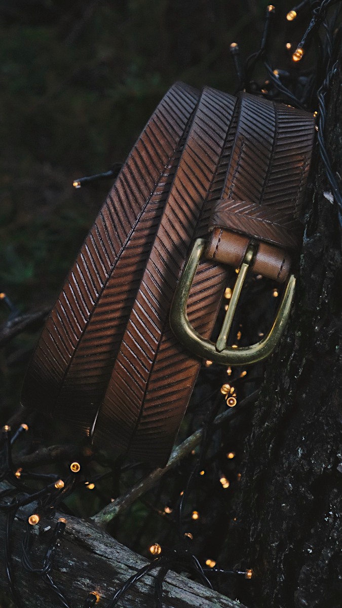 Brown belt is set onto the forest floor and leans a bit to the tree trunk. Scene is decorated by small sparkling lights and there is dark green background.