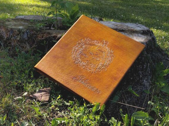 Yellow photo album is placed by the tree stump to show how the front cover looks. Album is surrounded by beautiful green grass and some white flowers.
