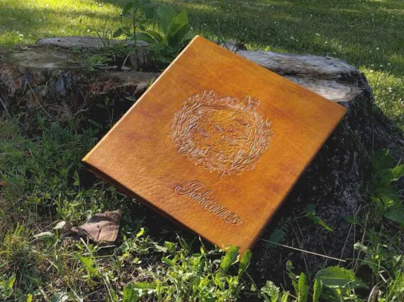 Yellow photo album is placed by the tree stump to show how the front cover looks. Album is surrounded by beautiful green grass and some white flowers.