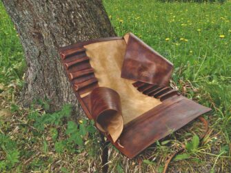 This photo shows the knife roll opened in full size. Leather roll is placed onto the grass besides a tree which is supporting it behind.