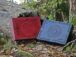 Large boxes in mahogany and blue are set onto the forest ground by the fallen and broken tree trunk. Both boxes have decorated beautiful lids. There are leaves all over the ground and some moss is visible between the tree roots.