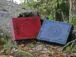 Large boxes in mahogany and blue are set onto the forest ground by the fallen and broken tree trunk. Both boxes have decorated beautiful lids. There are leaves all over the ground and some moss is visible between the tree roots.