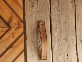 Indoor photo of the leather handle attached to the wooden door. Light brown handle with stitched edges.