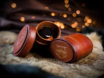 Brown oval shaped leather boxes. One of the boxes is opened and a watch is visible from the inside. The covers of the boxes are decorated by the watchmakers logos. 