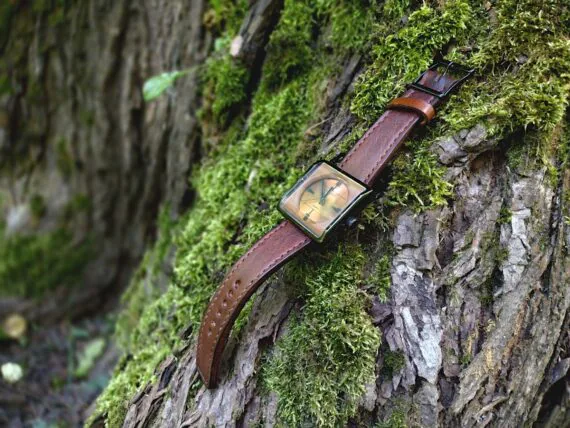 Watch with a strap is set onto the rough tree bark, surrounded by moss.