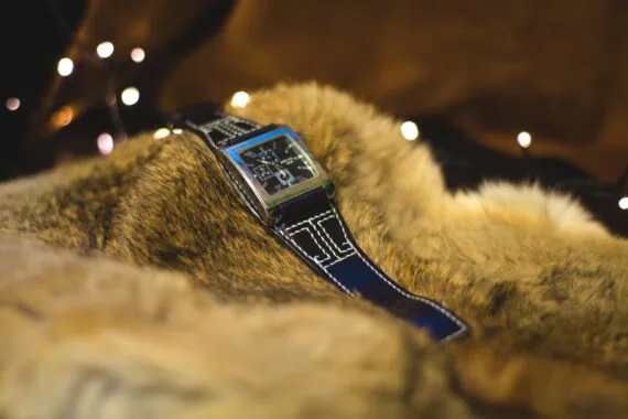 Photo shows a black wide watch strap that has stitches made by white thread on the light brown background.