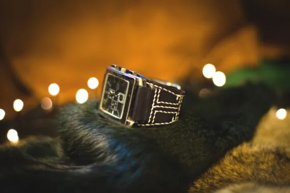 Photo shows a black wide watch strap that has stitches made by white thread on the light brown background.